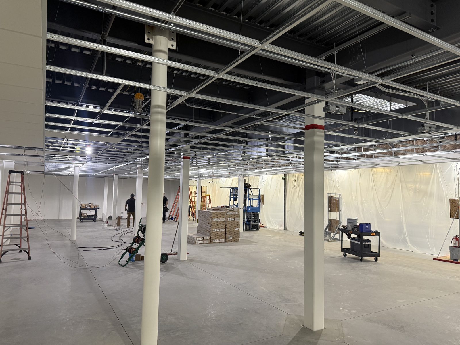 Suspended ceiling grid framed across the open floor with painted steel columns and electrical rough-in above on the CBR project in Tucson