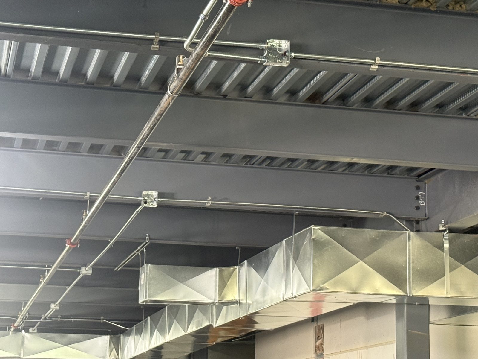 Electrical conduit, junction boxes, and fire-protection piping routed alongside spiral and rectangular HVAC ductwork on the CBR project