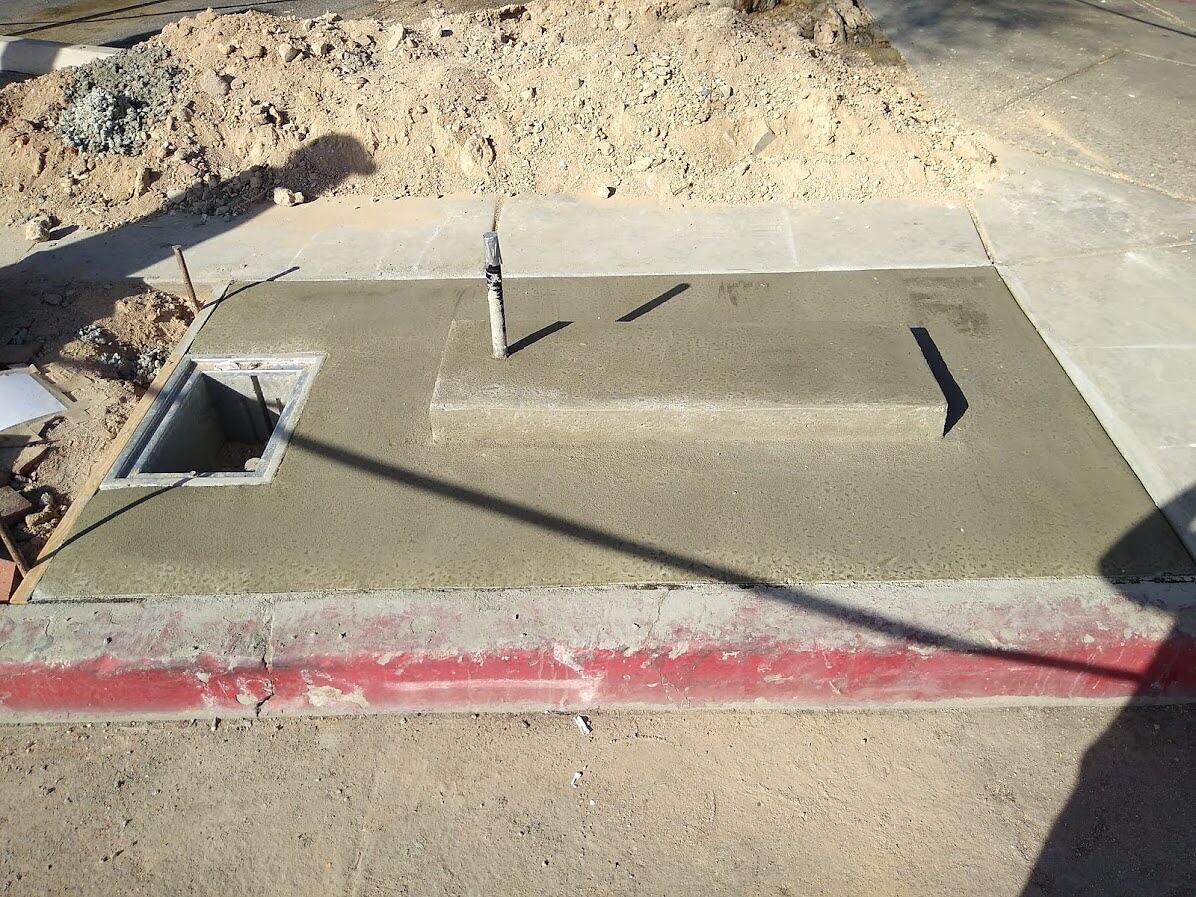Finished concrete kiosk foundation with raised plinth, conduit stub-up and open pull box in a restored sidewalk, Tucson