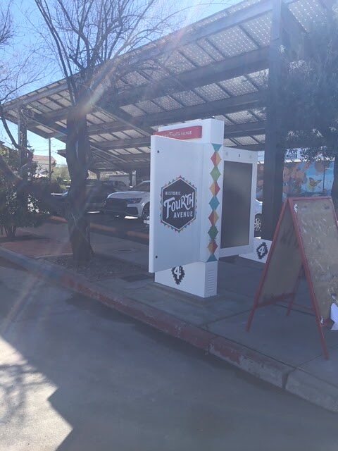 Historic Fourth Avenue kiosk installed on a sidewalk beneath a solar carport canopy in Tucson, Arizona