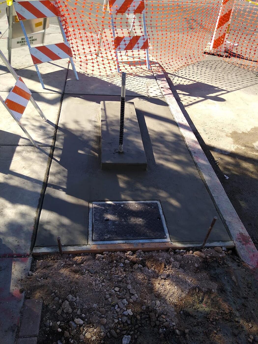 Completed kiosk pad with cast-in electric pull box lid and conduit stub-up behind construction barricades, Fourth Avenue, Tucson