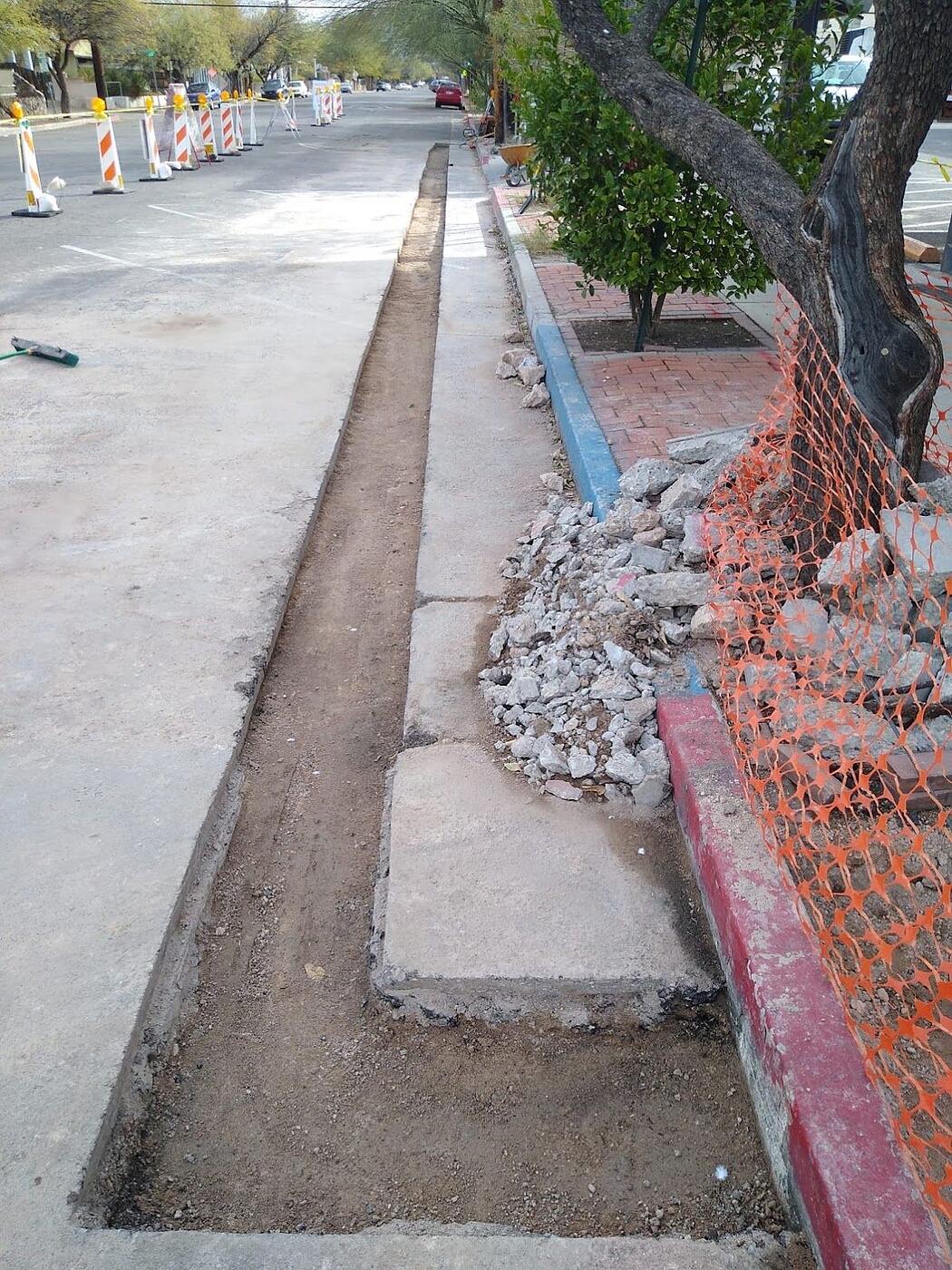 Open trench along the curb line on Fourth Avenue with traffic control barricades in place, Tucson, Arizona