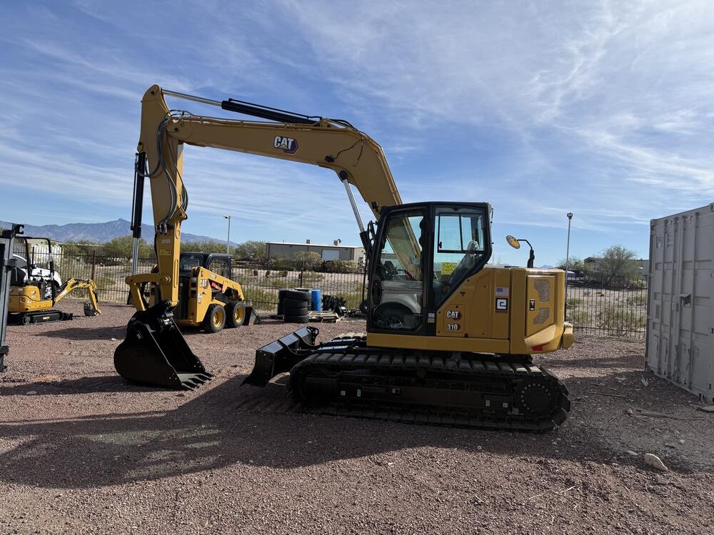 Arizona Electrical Solutions' owned Caterpillar fleet — a CAT 310 excavator with a skid steer and mini excavators staged at the Tucson equipment yard, Catalina Mountains in the background