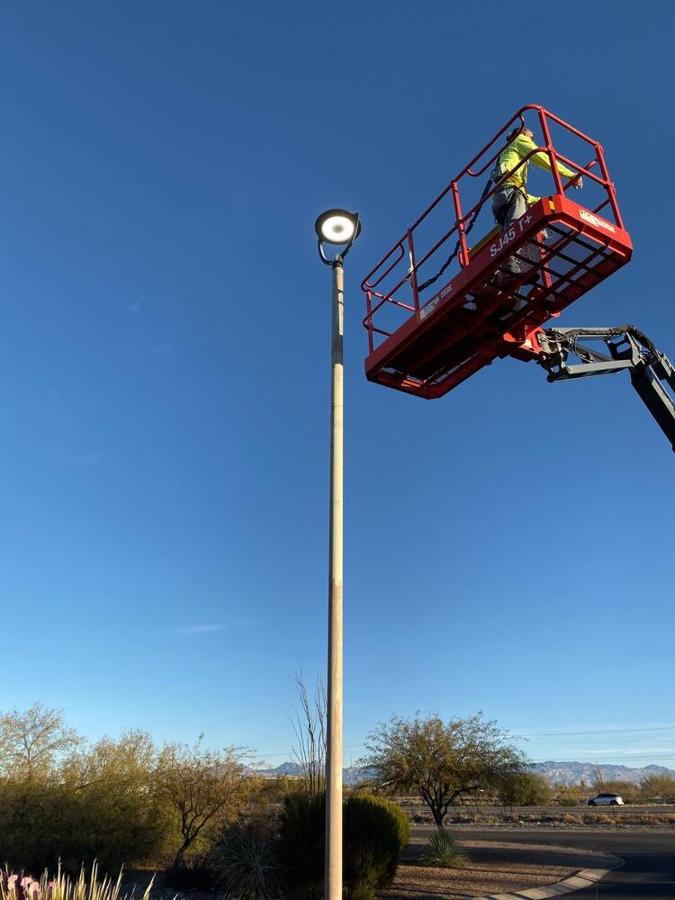 Electrician on a boom lift servicing a parking-lot pole light in Tucson, Arizona