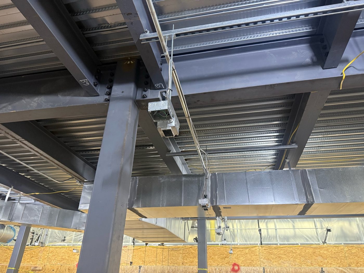 Bolted structural steel beam-to-column connection with an electrical junction box and conduit supports at a commercial design-build site in Tucson, Arizona